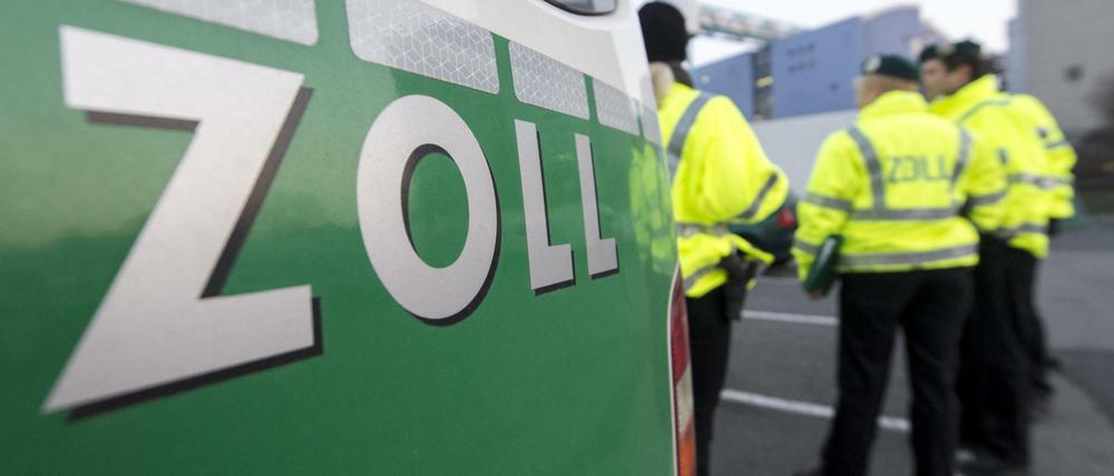Zollbeamte vor ihrem Dienstfahrzeug auf einem Parkplatz.