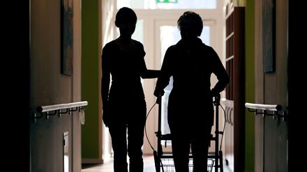 Eine Pflegekraft begleitet die Bewohnerin eines Altenheims beim Gang über den Flur.