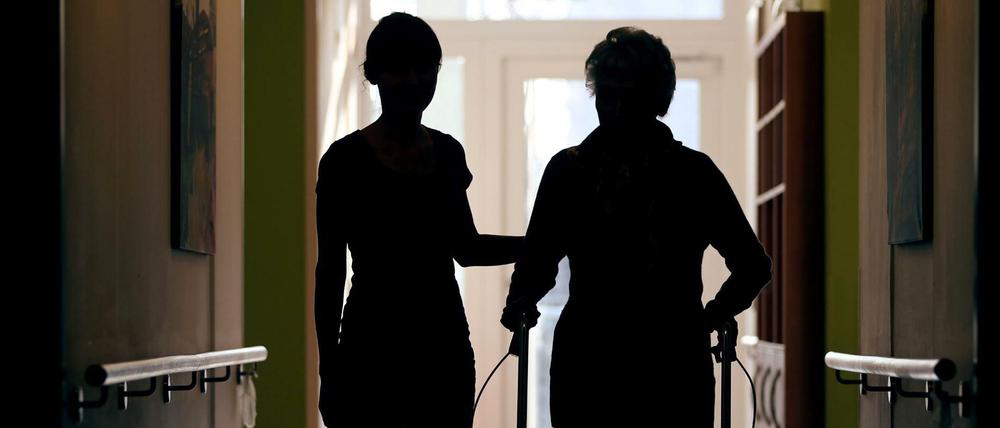 Eine Pflegekraft begleitet die Bewohnerin eines Altenheims beim Gang über den Flur.