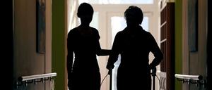 Eine Pflegekraft begleitet die Bewohnerin eines Altenheims beim Gang über den Flur.