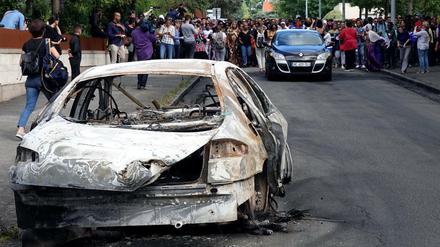 Ein ausgebranntes Auto im französischen Nantes, aufgenommen am 5. Juli. Dahinter laufen Teilnehmer eines Protestmarsches.