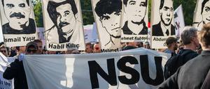 Demonstrierende halten bei einer Kundgebung Schilder mit Porträts der NSU-Opfer.