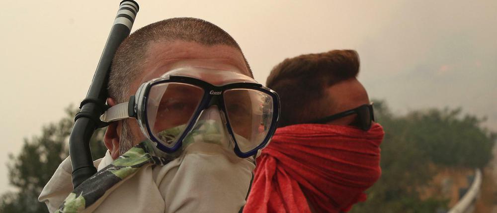 Zwei Männer schützen sich nahe dem Ferienort Kineta mit Tüchern und einem Schnorchel vor dem Rauch eines Großbrandes.