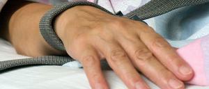 Eine mit einem Textilband festgebundene Hand eines Patienten.