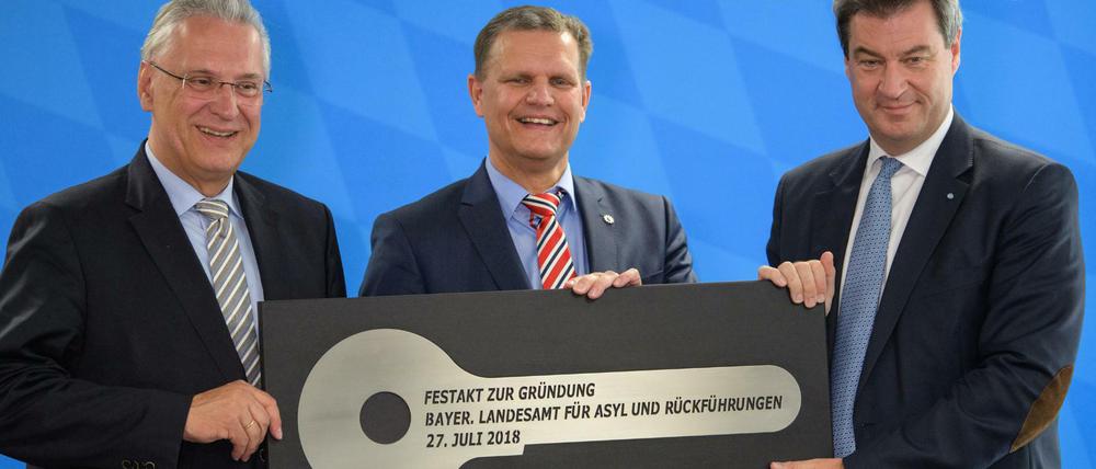 Joachim Herrmann (CSU, l), Innenminister von Bayern, und Markus Söder (CSU, r), Ministerpräsident von Bayern, überreichen bei der Gründungsfeier des Landesamtes für Asyl und Rückführungen im Transitzentrum Manching den symbolischen Schlüssel an Thomas Hampel, Präsident des neuen Bayerischen Asyl-Landesamts. Mit dem Landesamt sollen zentral für Bayern Passbeschaffung, Rückführung und Förderung der freiwilligen Ausreise sowie Maßnahmen gegen ausländische Gefährder und Straftäter verbessert werden.