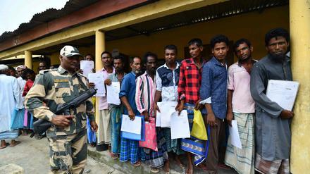 Unter den Augen eines bewaffneten Wachmanns stehen Menschen im nordindischen Bundesstaat Assam Schlange, um nachzuschauen, ob ihre Namen im neuen Bürgerregister stehen.