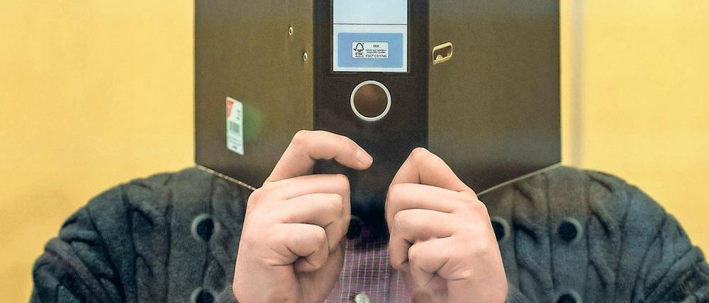 Der Angeklagte Nils D. steht am 20.01.2016 in Düsseldorf (Nordrhein-Westfalen) mit einem Aktenordner vor dem Gesicht im Gerichtsaal. Der mutmaßlicher Terrorist des «Islamischen Staats» (IS) muss auf die Anklagebank des Oberlandesgerichts. Der 25-Jährige aus Dinslaken soll in Syrien einer Spezialeinheit des IS angehört haben, die Deserteure und Abweichler aufspüren sollte. Foto: Federico Gambarini/dpa +++(c) dpa - Bildfunk+++
