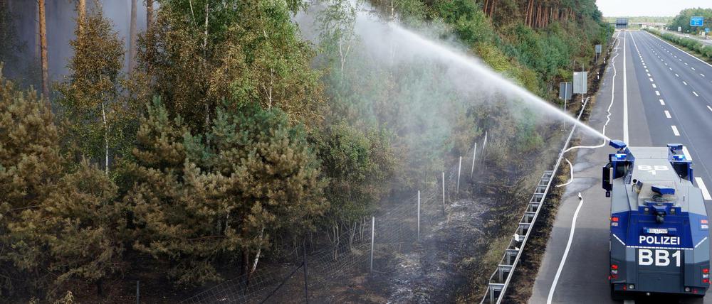 Ein Wasserwerfer der Polizei löscht am Rande eines Waldgebietes auf der Autobahn.