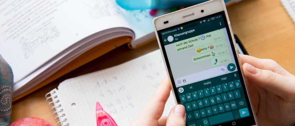Eine Schülerin sitzt mit ihrem Handy und ihren Schulsachen an einem Schreibtisch.