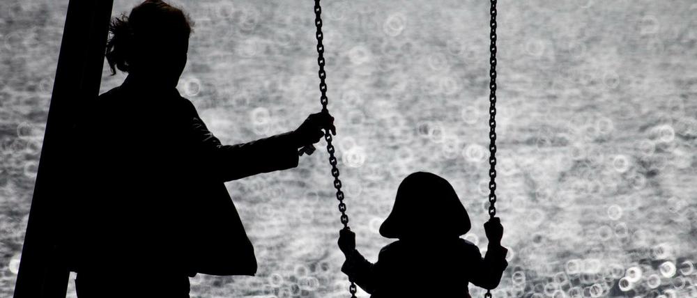 Eine Mutter schaukelt ihr Kind auf einem kleinen Spielplatz. (Symbolbild)