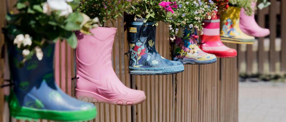 Gummistiefel mit Blumen am Zaun eines Kindergartens. 