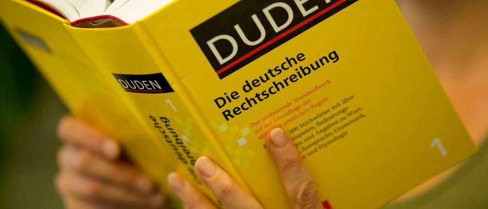 Eine Frau hält einen Duden in den Händen.