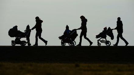 Mütter schieben ihre Kinderwagen eine Landstraße entlang.