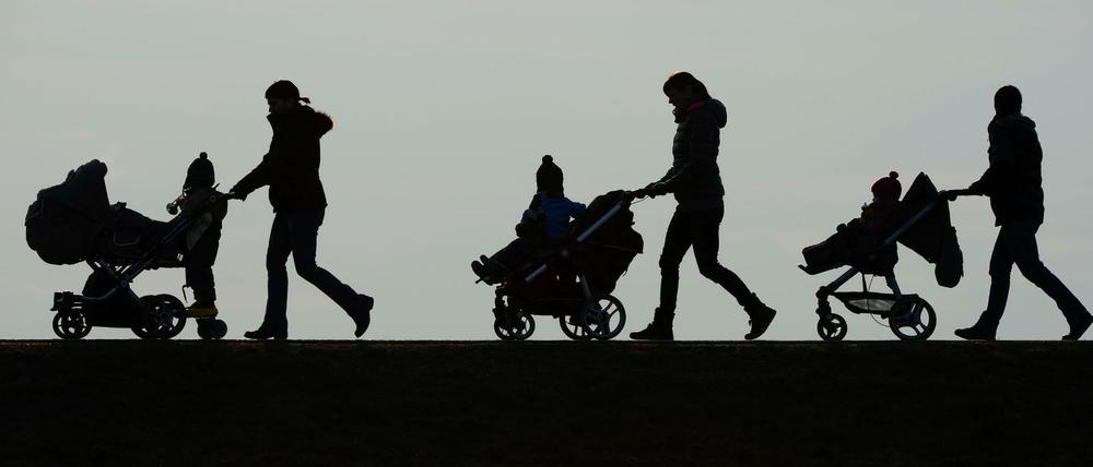 Mütter schieben ihre Kinderwagen eine Landstraße entlang.