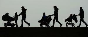 Mütter schieben ihre Kinderwagen eine Landstraße entlang.
