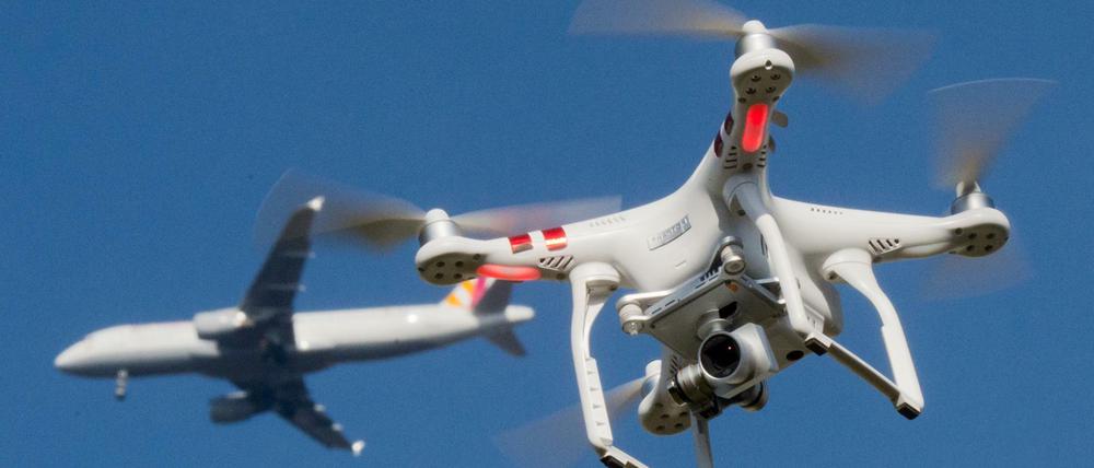 Eine private Drohne fliegt in knapp 10 Metern Flughöhe über einem Garten, als in weiter Entfernung ein Flugzeug beim Anflug auf den Flughafen Düsseldorf zu sehen ist.