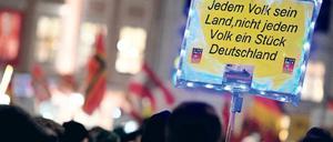 Teilnehmende einer Pegida-Demonstration halten ein Schild mit der Aufschrift "Jedem Volk sein Land, nicht jedem Volk ein Stück Deutschland".