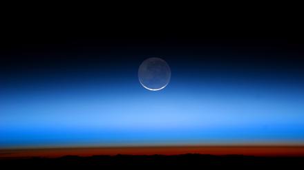 Der Mond, aufgenommen von der Internationalen Raumstation. Die helle Sichel wird von der Sonne beschienen, der blasser erscheinende Teil von der Erde.