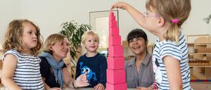 Kitakinder bauen einen Turm aus Klötzchen, zwei Erzieherinnen schauen zu.