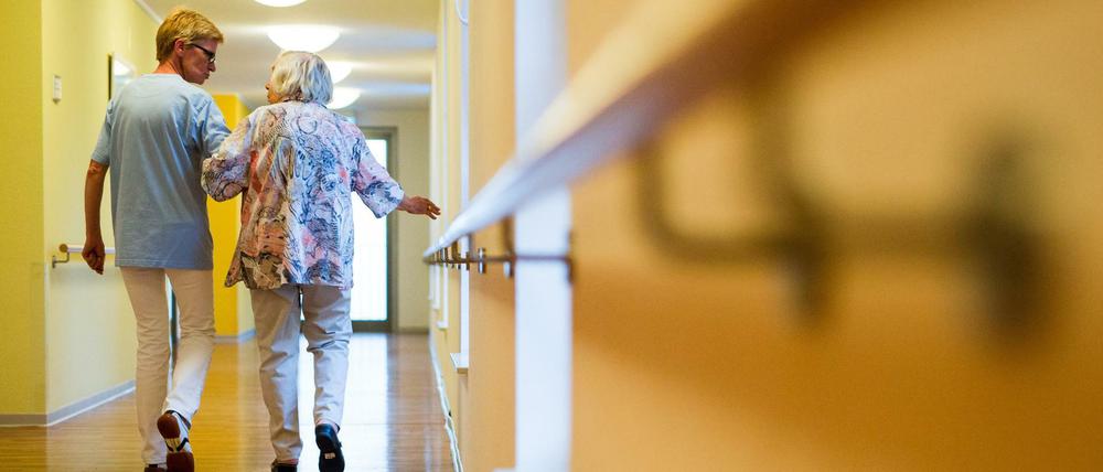 Eine Pflegekraft geht in einem Pflegeheim mit einer älteren Dame über einen Korridor.