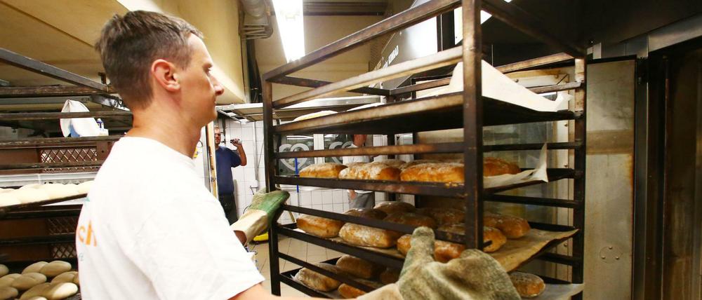 Ein Bäcker holt frisch gebackene Brote aus einem Backofen in einer Bäckerei.
