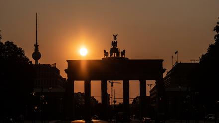 Das Brandenburger Tor und der Fernsehturm sind im Gegenlicht der aufgehenden Sonne nur als Silhouette zu erkennen.  