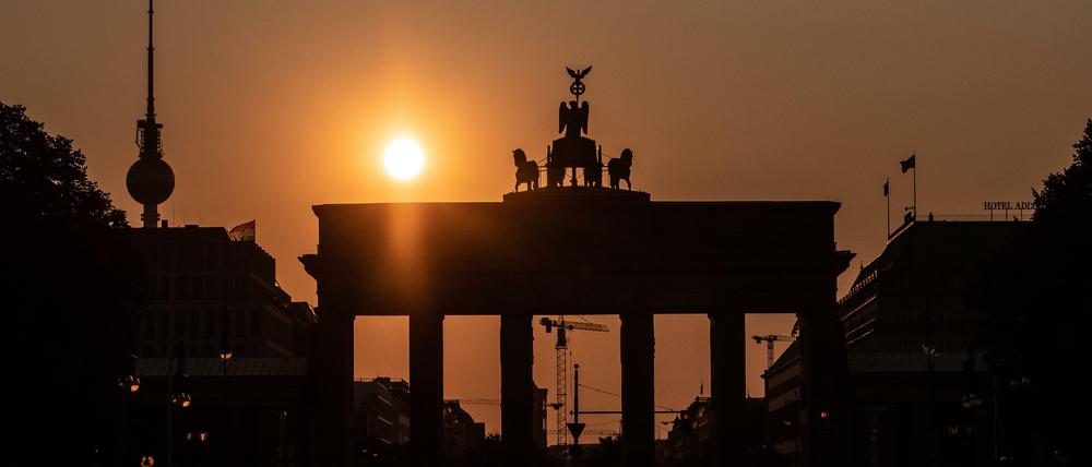 Das Brandenburger Tor und der Fernsehturm sind im Gegenlicht der aufgehenden Sonne nur als Silhouette zu erkennen.  