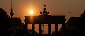 Das Brandenburger Tor und der Fernsehturm sind im Gegenlicht der aufgehenden Sonne nur als Silhouette zu erkennen.  