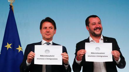 Ministerpräsident Giuseppe Conte und Innenminister Matteo Salvini halten Papiere mit dem Titel des Dekrets über den Umgang mit Migranten hoch.