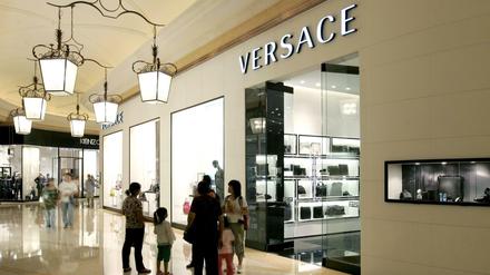 Besucher gehen vor einem Versace-Shop in einem Luxus-Einkaufszentrum in Macao in China.
