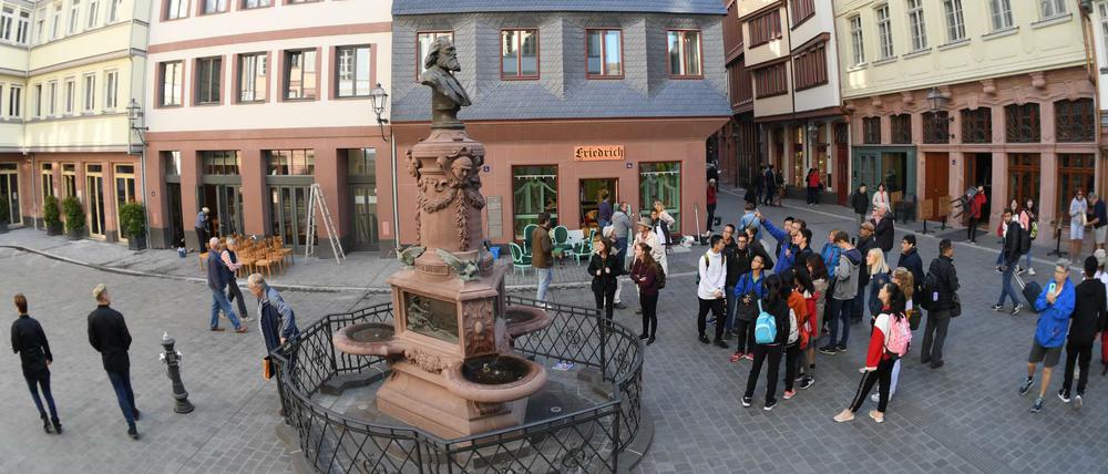 Touristen stehen auf dem Hühnermarkt der neuen Frankfurter Altstadt am restaurierten Friedrich-Stoltze-Brunnen.