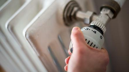 Eine Frau dreht am Thermostat einer Heizung.