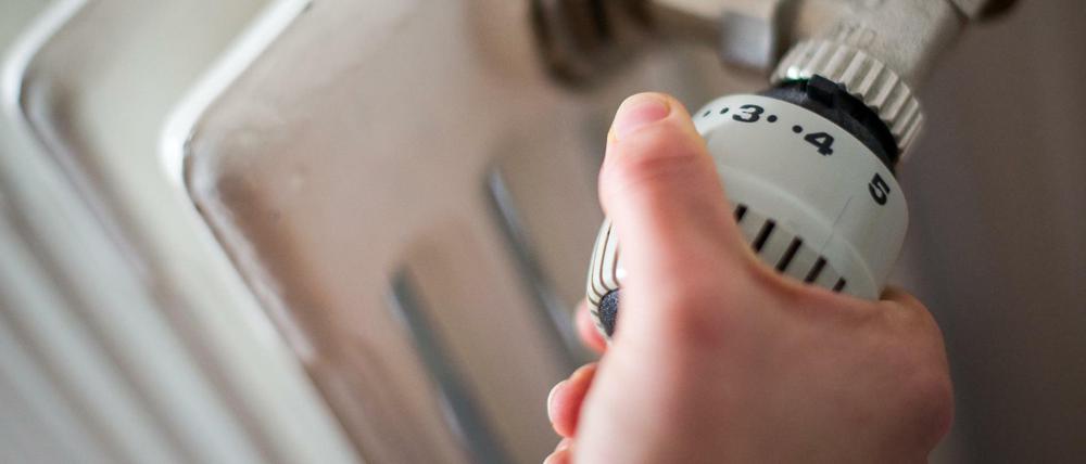 Eine Frau dreht am Thermostat einer Heizung.