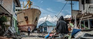 Indonesien, Palu: Menschen gehen eine Straße entlang in der Nähe des Ortes, wo ein Schiff während des Tsunamis an Land gespült wurde. Rund 5000 Menschen werden nach den Erdbeben und dem Tsunami in Indonesien noch immer vermisst. 