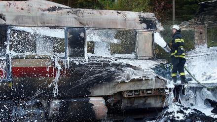 Ein Feuerwehrmann löscht die Flammen im ausgebrannten Zug.
