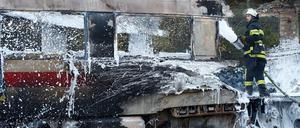 Ein Feuerwehrmann löscht die Flammen im ausgebrannten Zug.