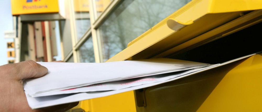 Briefe werden in einen Briefkasten geworfen.