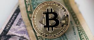 Archivbild einer Bitcoin Münze, die auf einem Dollar Geldscheinen liegt (gestellte Szene).