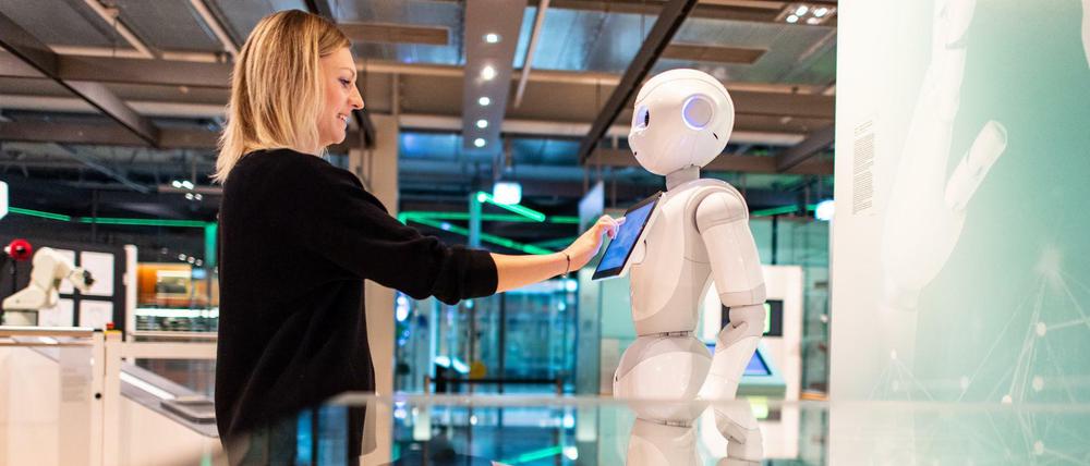 Die Kuratorin Judith Spickermann steht in der Ausstellung: "Künstliche Intelligenz und Robotik" im Heinz Nixdorf MuseumsForum vor einem Serviceroboter Namens Pepper.