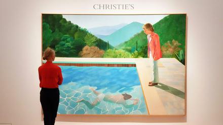 Eine Frau steht vor David Hockneys Gemälde "Portrait of an Artist (Pool with Two Figures)" im Auktionshaus Christie's.