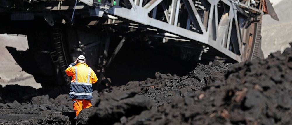 Nordrhein-Westfalen, Grevenbroich: Ein Mitarbeiter von RWE Power steht im Rheinischen Braunkohlerevier im Tagebau Garzweiler vor einem Schaufelradbagger, der Braunkohle abträgt.