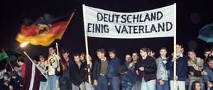 Wendezeit: Berliner mit Fahne und Transparent "Deutschland Einig Vaterland" im Dezember 1989 auf der Mauer am Brandenburger Tor.