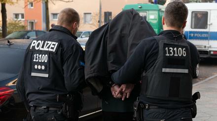 Polizeibeamte führen mit Handschellen einen festgenommenen Mann nach einer Razzia in einem Wohnhaus in Tempelhof ab. 