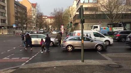 Auto-Rückstau in Fußgängerfurt bei grüner Fußgängerampel, Schulkinder und Eltern müssen sich zwischen Autos durchschlängeln.