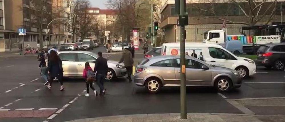 Auto-Rückstau in Fußgängerfurt bei grüner Fußgängerampel, Schulkinder und Eltern müssen sich zwischen Autos durchschlängeln.