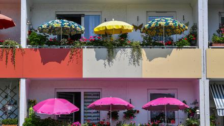 Bunte Sonnenschirme leuchten in der Mittagssonne auf Balkons eines Mehrfamilienhauses in Brandenburg.