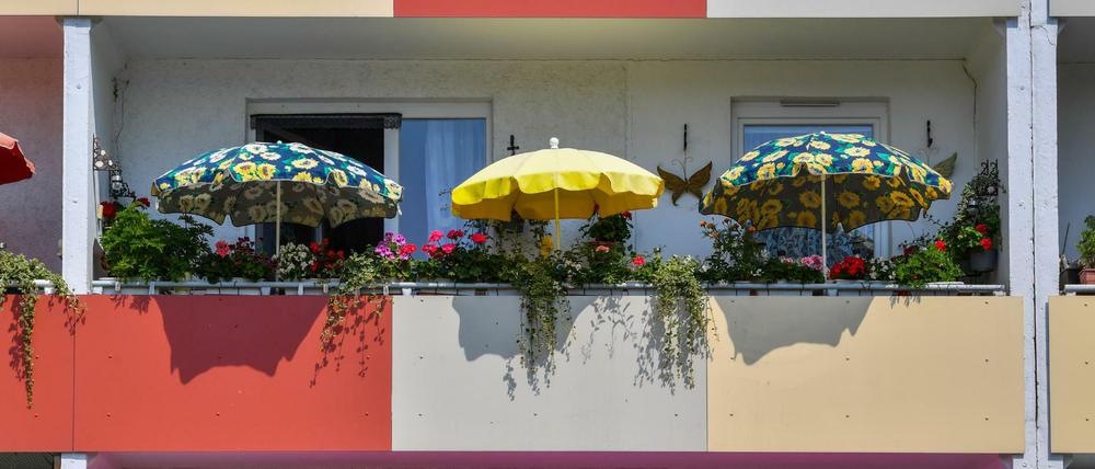 Bunte Sonnenschirme leuchten in der Mittagssonne auf Balkons eines Mehrfamilienhauses in Brandenburg.