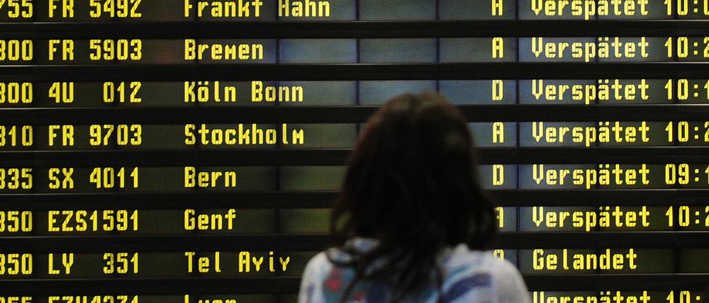 Eine Frau steht auf dem Flughafen Berlin-Schönefeld vor einer Anzeigetafel, auf der verspätete Flüge aufgelistet werden.