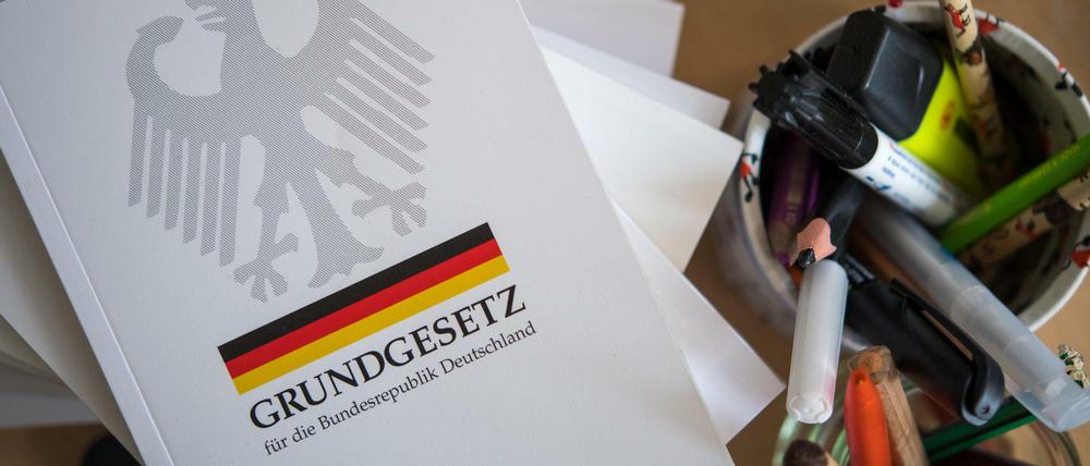Eine Ausgabe des Grundgesetzes der Bundesrepublik Deutschland liegt auf einem Tisch neben Schreibutensilien.