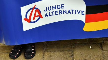 Ein Mann in schwarzen Sandalen hält ein Plakat der AfD-Jugendorganisation Junge Alternative (JA). 